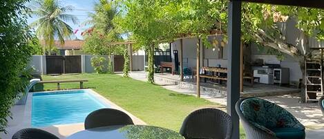 Un espacio al aire libre techado con piscina, asientos y vista al jardín trasero.