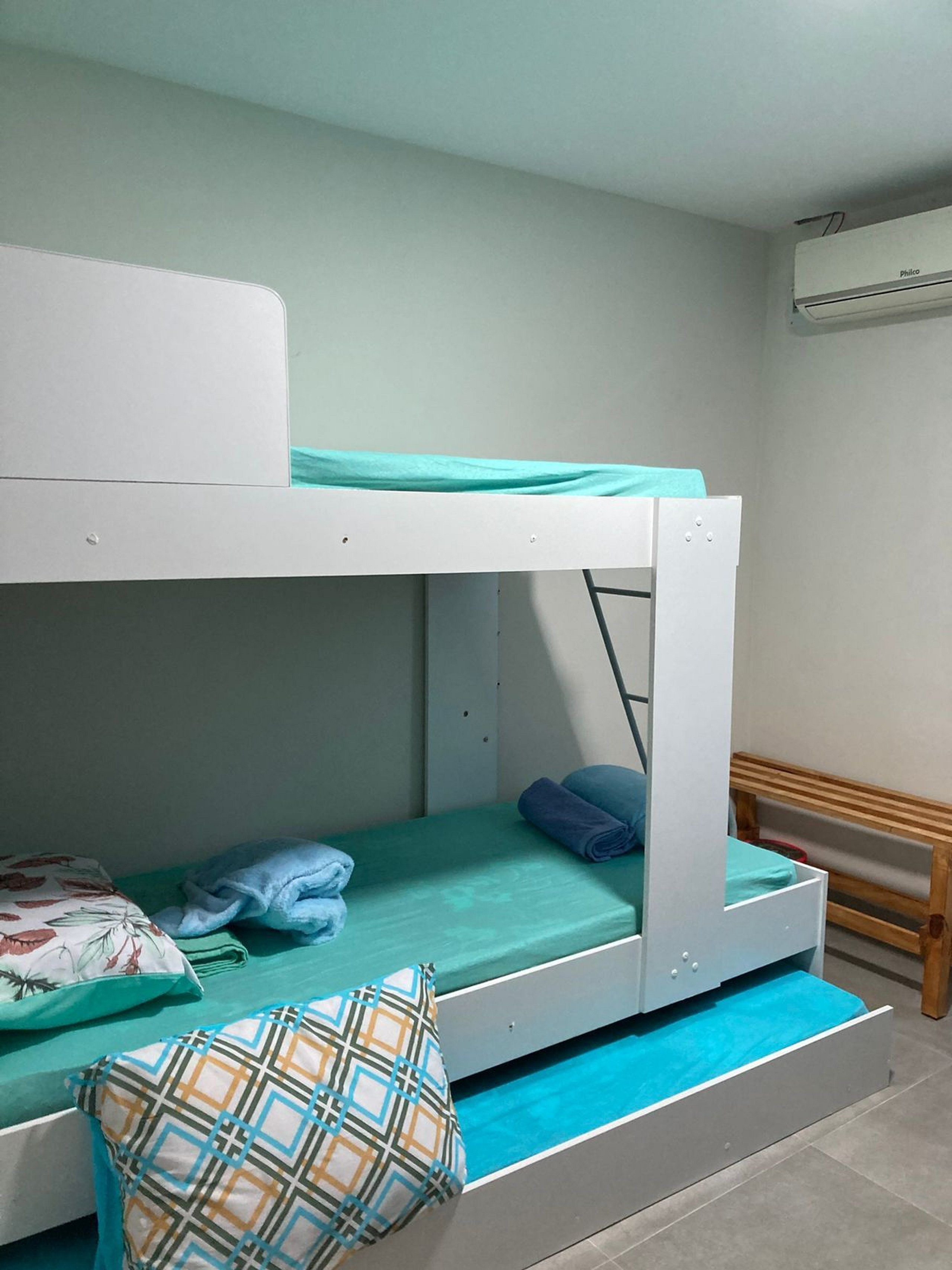 A bunk bed with a mattress and pillows, a wooden bench, and an air conditioning unit.