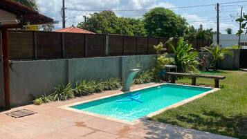 Piscina com deck revestido, rodeada por um muro baixo e vegetação.