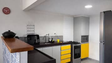 Una cocina moderna con estufa, microondas y refrigerador. Hay una encimera de madera y un lavamanos con grifo.