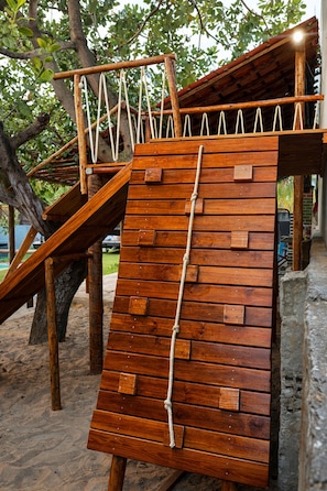 A wooden climbing structure with a rope ladder, set against a backdrop of trees and a building. - Porto de Galinhas - Serrambi - Loctemp (Ipojuca)