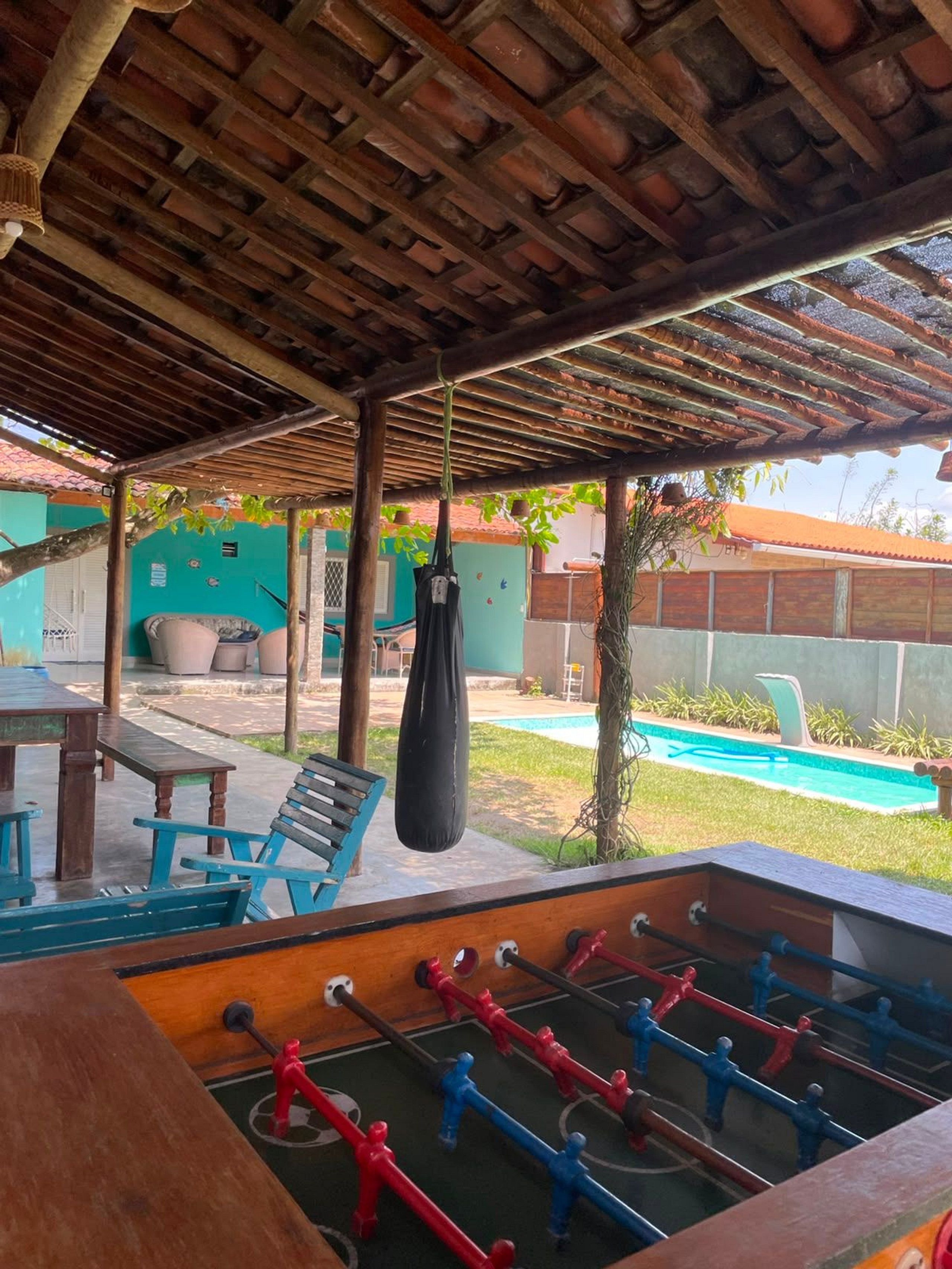 Un espace extérieur aménagé en terrasse, avec une table de baby-foot, un sac de frappe suspendu et une piscine en arrière-plan.