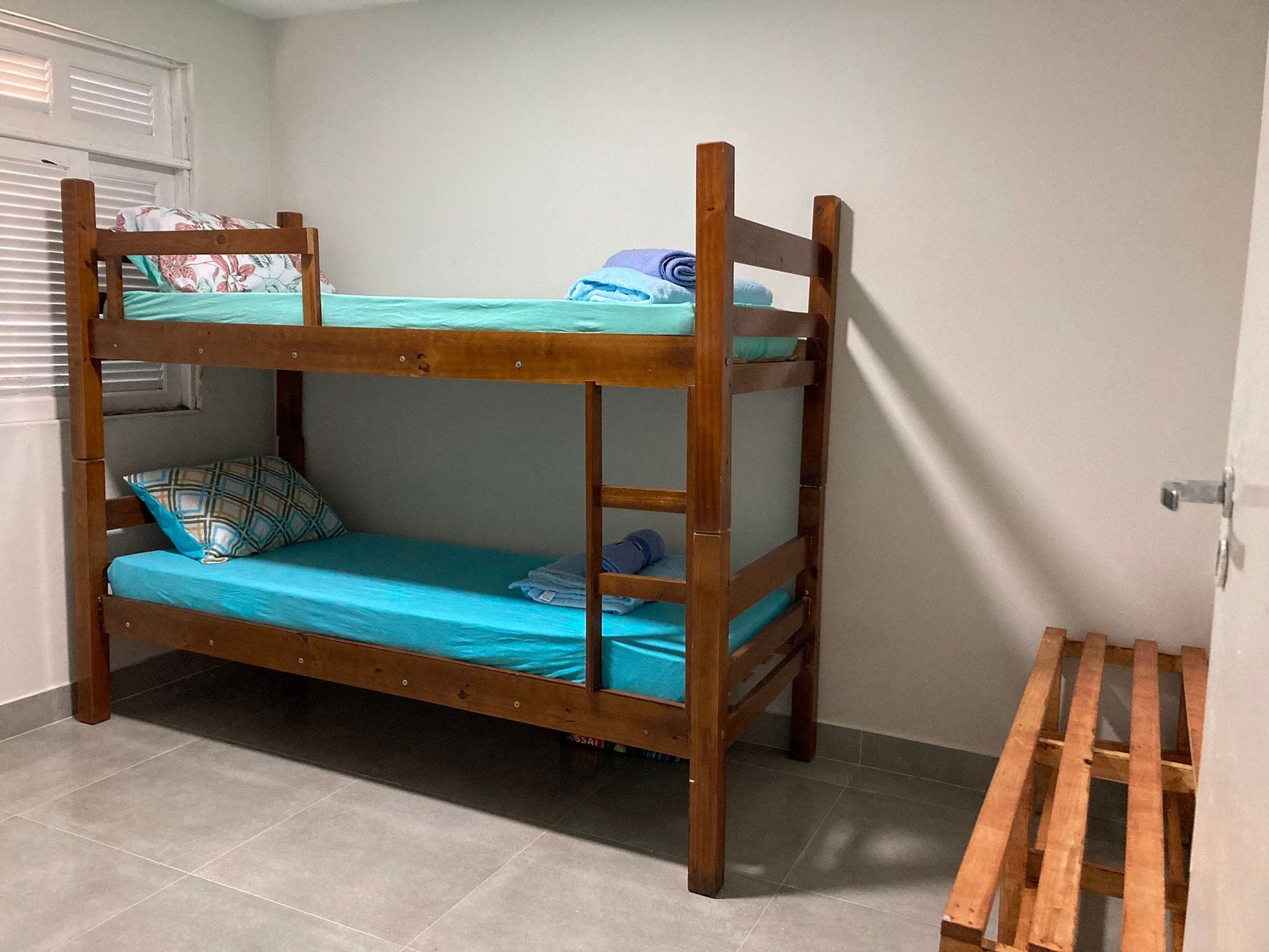 Ein Etagenbett mit Holzbettgestell, ein unteres Bett mit blauer Matratze und ein Kopfkissen mit Karomuster.