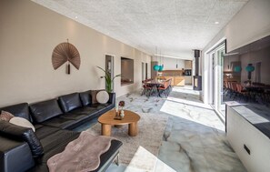 A modern living room with a black leather sofa, a wooden coffee table, and a dining area with a marble floor. - 4 bedroom cozy home in Thyholm (Thyholm)