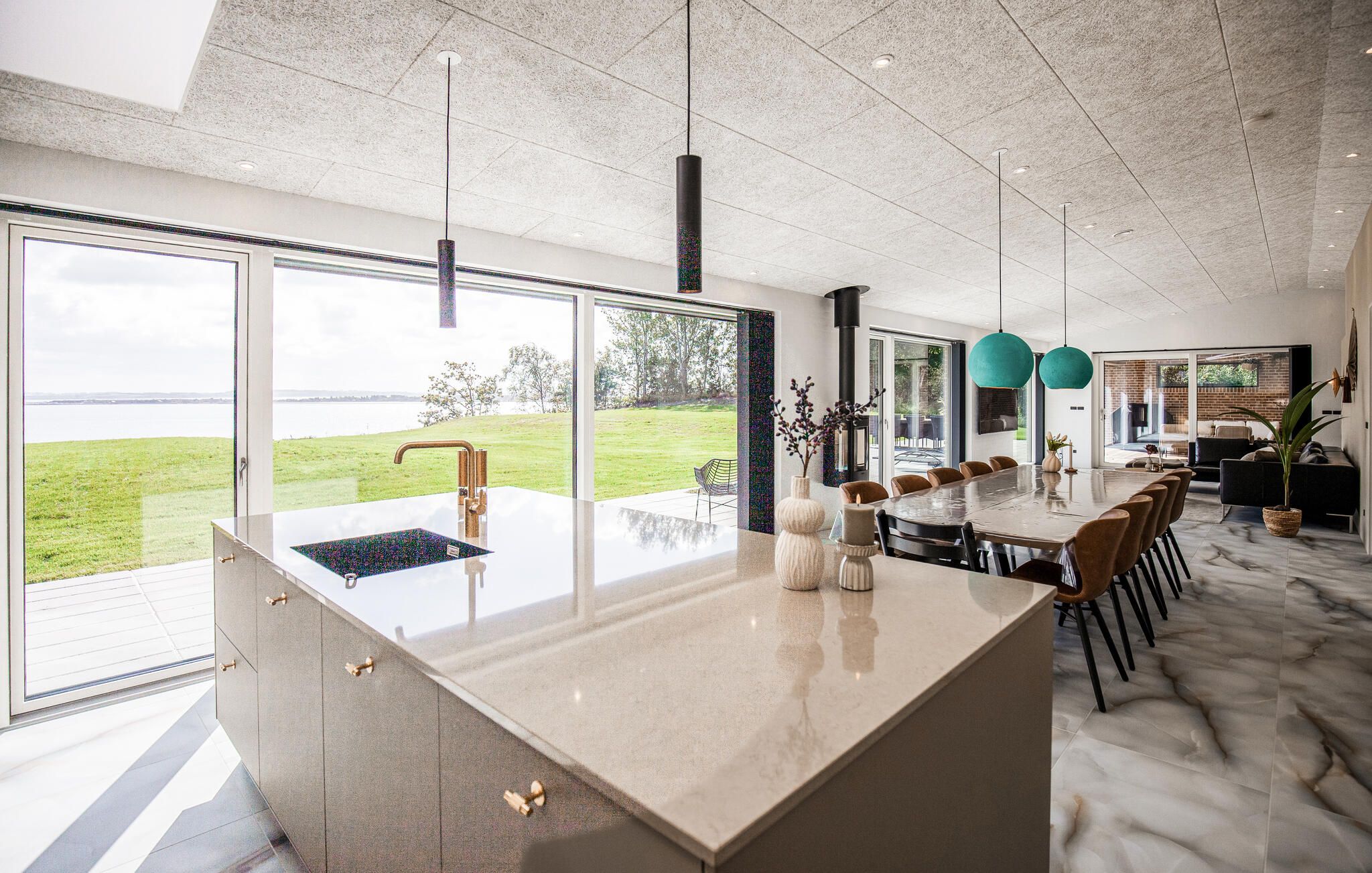 A modern kitchen with a large island, a view of the outdoors, and a dining area with a long table and chairs.