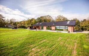 A modern house with a large glass facade, a spacious lawn, and a clear sky. - 4 bedroom cozy home in Thyholm (Thyholm)