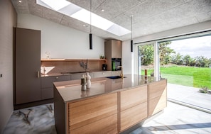 A modern kitchen with a large island, built-in appliances, and a view of a green landscape. - 4 bedroom cozy home in Thyholm (Thyholm)