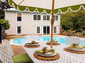 A poolside dining area with white chairs and tables, a pool, and a house with a green awning in the background. - NEW! Romantic country retreat in the heart of wine & hunt country (Upperville)