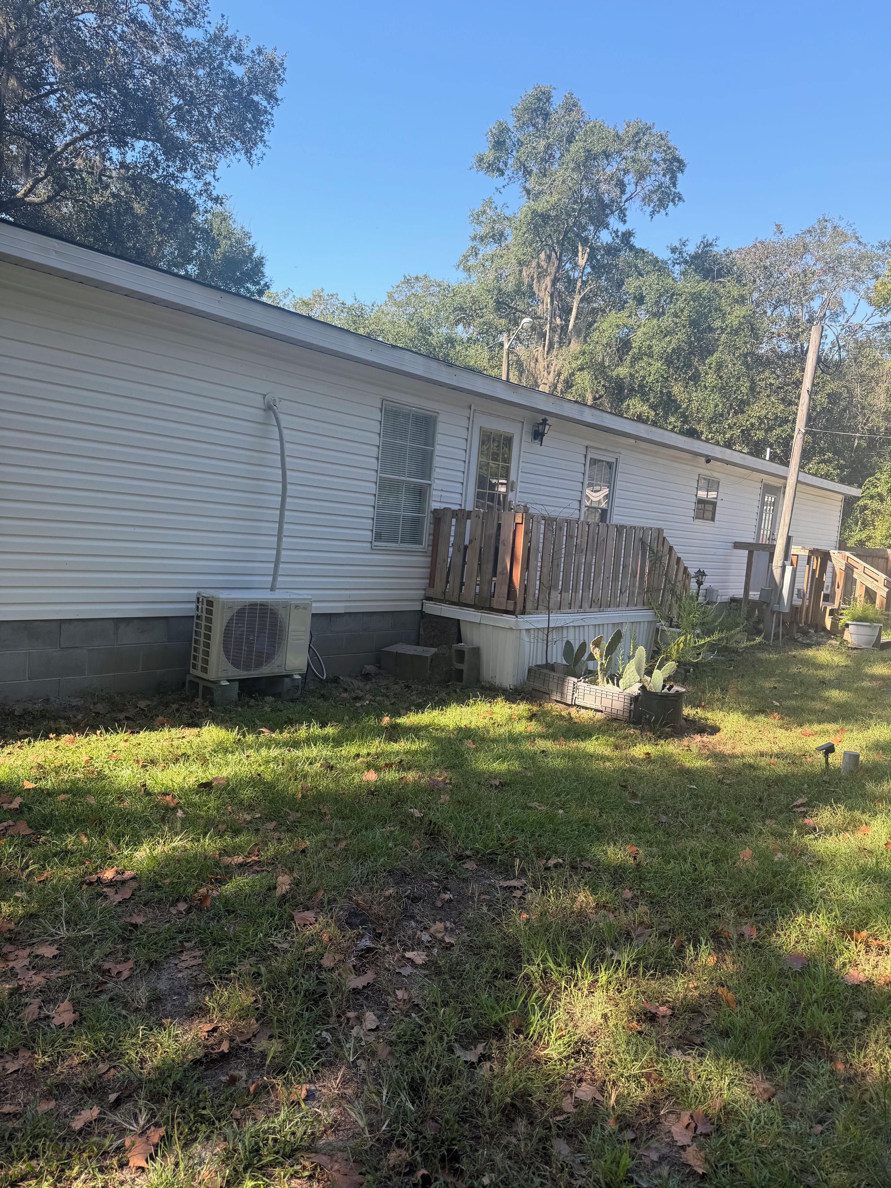 Una casa móvil con patio cercado, unidad de aire acondicionado exterior y una pequeña zona de porche.