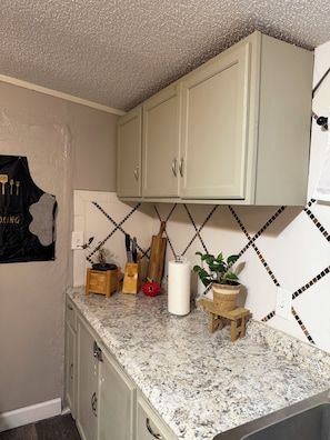 Eine Küche mit weißen Schränken, einer Arbeitsplatte aus Granit und einer Küchenrückwand mit geometrischem Muster.