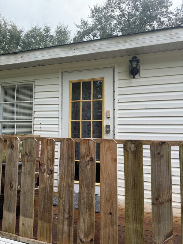 A white building with a front door, a window with a floral pattern, and a wooden fence.