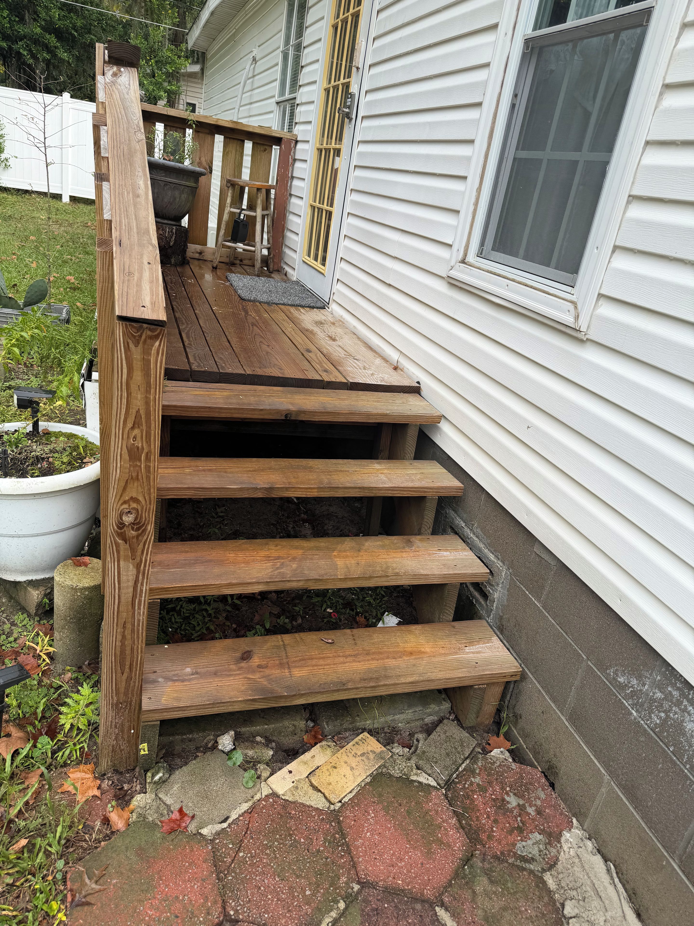 A wooden staircase leading to a porch with a potted plant and a window.