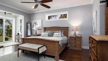 A bedroom with a wooden bed, bedside tables, a bench, a ceiling fan, and a large window.