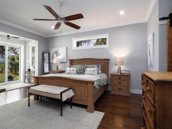 A bedroom with a wooden bed, bedside tables, a bench, a ceiling fan, and a large window.