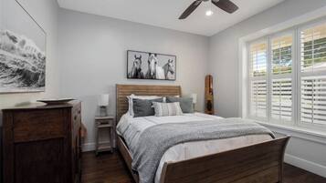 A bedroom with a wooden bed, a nightstand, a desk, a ceiling fan, and a window with blinds.