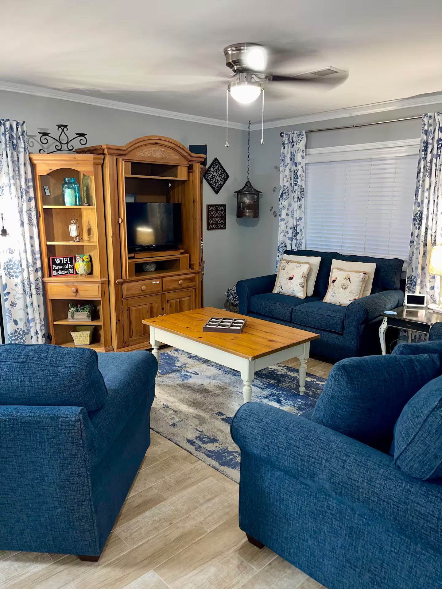 A living room with a wooden entertainment center, a blue sofa set, and a coffee table.
