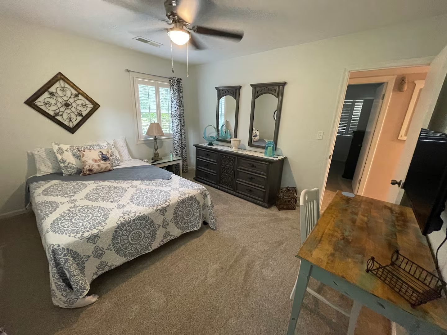 A bedroom with a bed, dresser, vanity, and a ceiling fan.