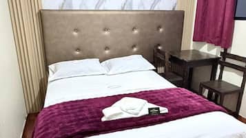 A bed with a headboard, a table, and a chair in a room with a patterned wall.