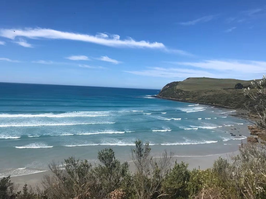 A coastal landscape with a beach, ocean waves, and a grassy hill.
