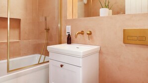 Un bagno con lavandino bianco, accessori dorati, doccia e una pianta in vaso.