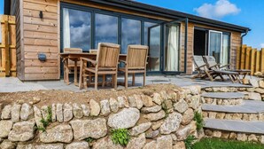 Una baita di legno con un muro in pietra, un patio con sedie e una porta vetrata che dà su un'area coperta.