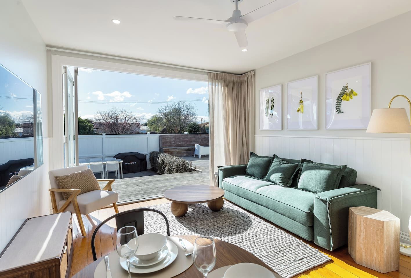 Ein modernes Wohnzimmer mit einem grünen Sofa, einem Esstisch mit Tellern und Gläsern und Blick durch große Fenster.