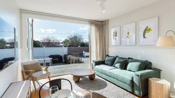 Ein modernes Wohnzimmer mit einem grünen Sofa, einem Esstisch mit Tellern und Gläsern und Blick durch große Fenster.