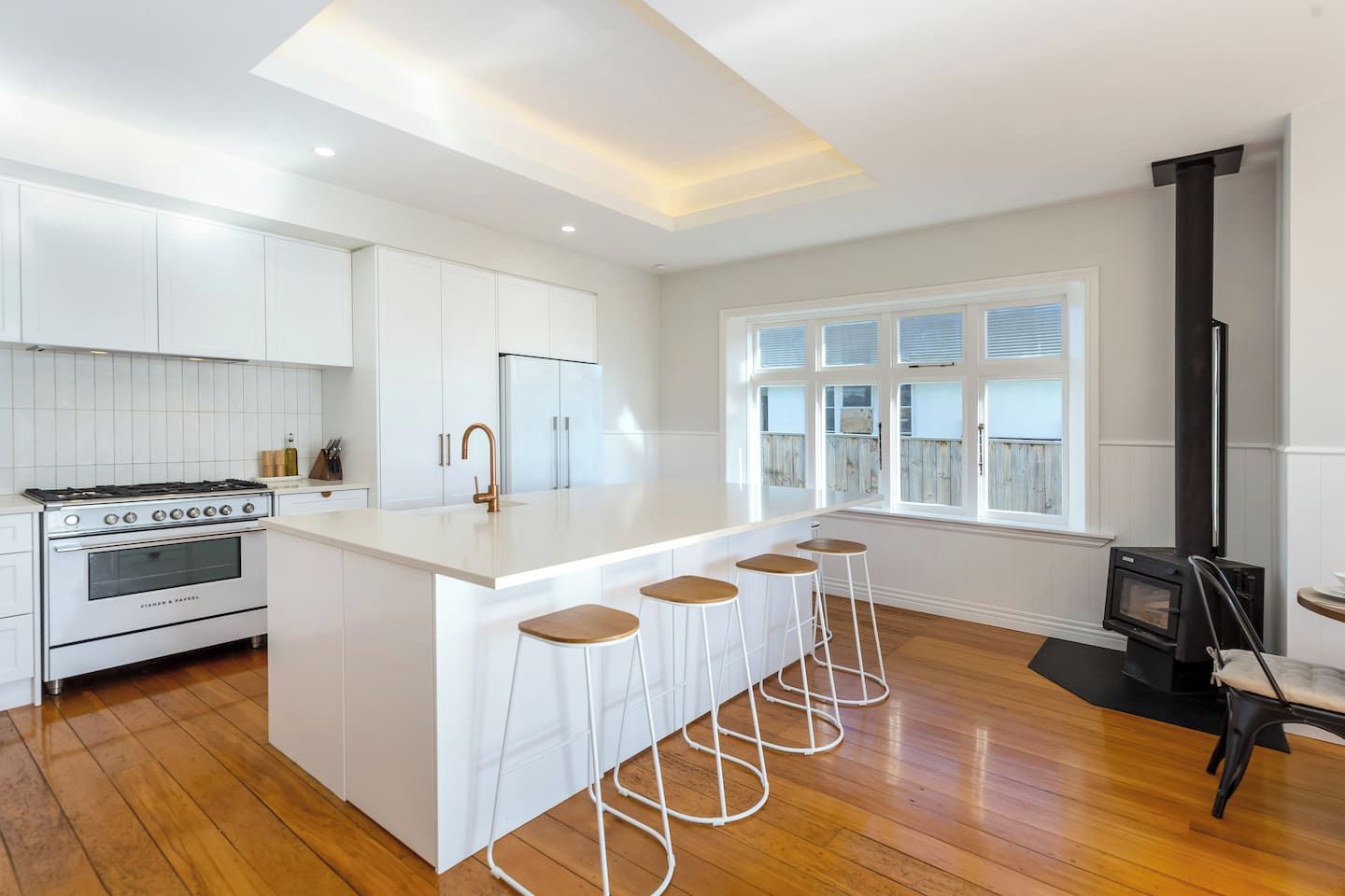 A modern kitchen with a central island, bar stools, a stove, and a wood-burning stove.
