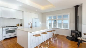 A modern kitchen with a central island, bar stools, a stove, and a wood-burning stove.