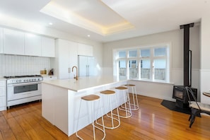 A modern kitchen with a central island, bar stools, a stove, and a wood-burning stove.