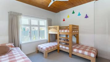A bedroom with two bunk beds, a window with curtains, a ceiling fan, and a wall with colorful triangular decorations.