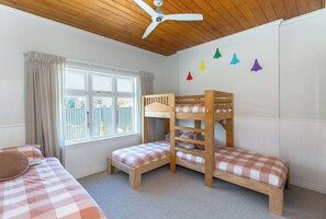 A bedroom with two bunk beds, a window with curtains, a ceiling fan, and a wall with colorful triangular decorations.