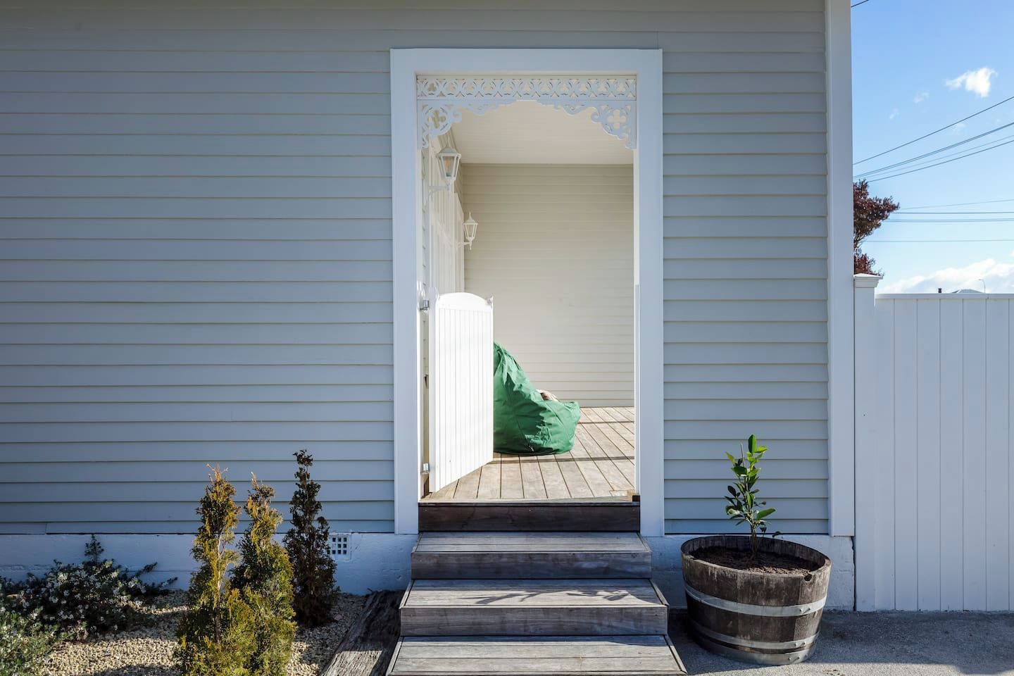 A house with a white exterior, a wooden front porch, and a green bag on the steps.