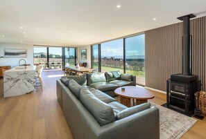 A modern living room with a large sofa, a dining area, and a fireplace. - Three Ranges | private vineyard + spa (Martinborough)