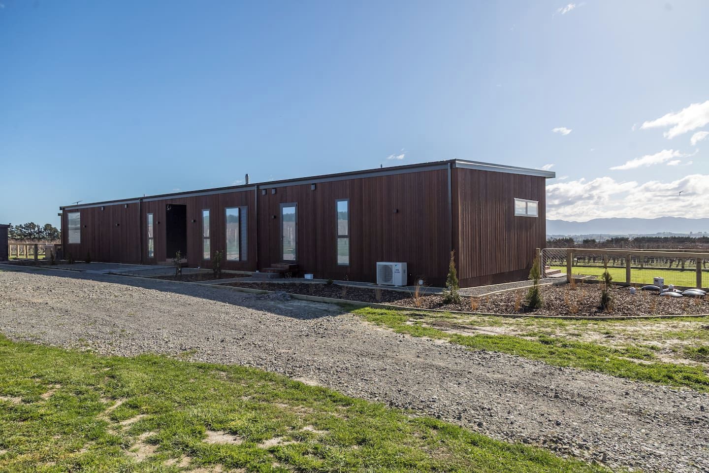 Een modern gebouw met een plat dak, grote ramen en een grindpad.
