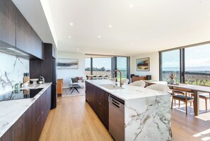 A modern kitchen with a marble countertop, wooden cabinets, and a large island with a sink. - Three Ranges | private vineyard + spa (Martinborough)