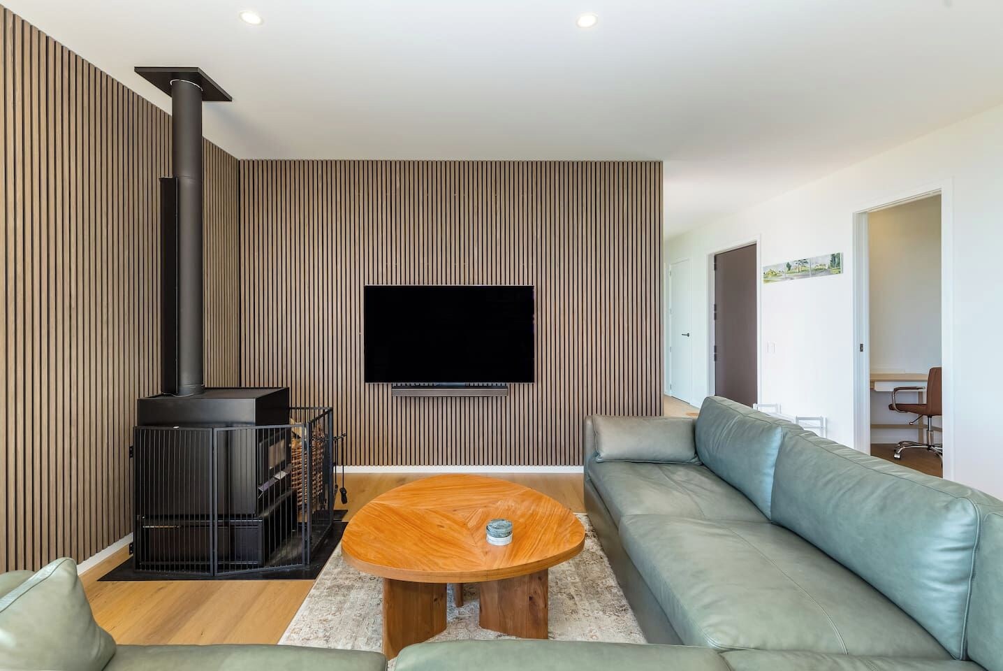 A modern living room with a sofa, a coffee table, a fireplace, and a flat-screen TV mounted on the wall.