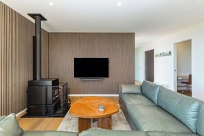 A modern living room with a sofa, a coffee table, a fireplace, and a flat-screen TV mounted on the wall. - Three Ranges | private vineyard + spa (Martinborough)
