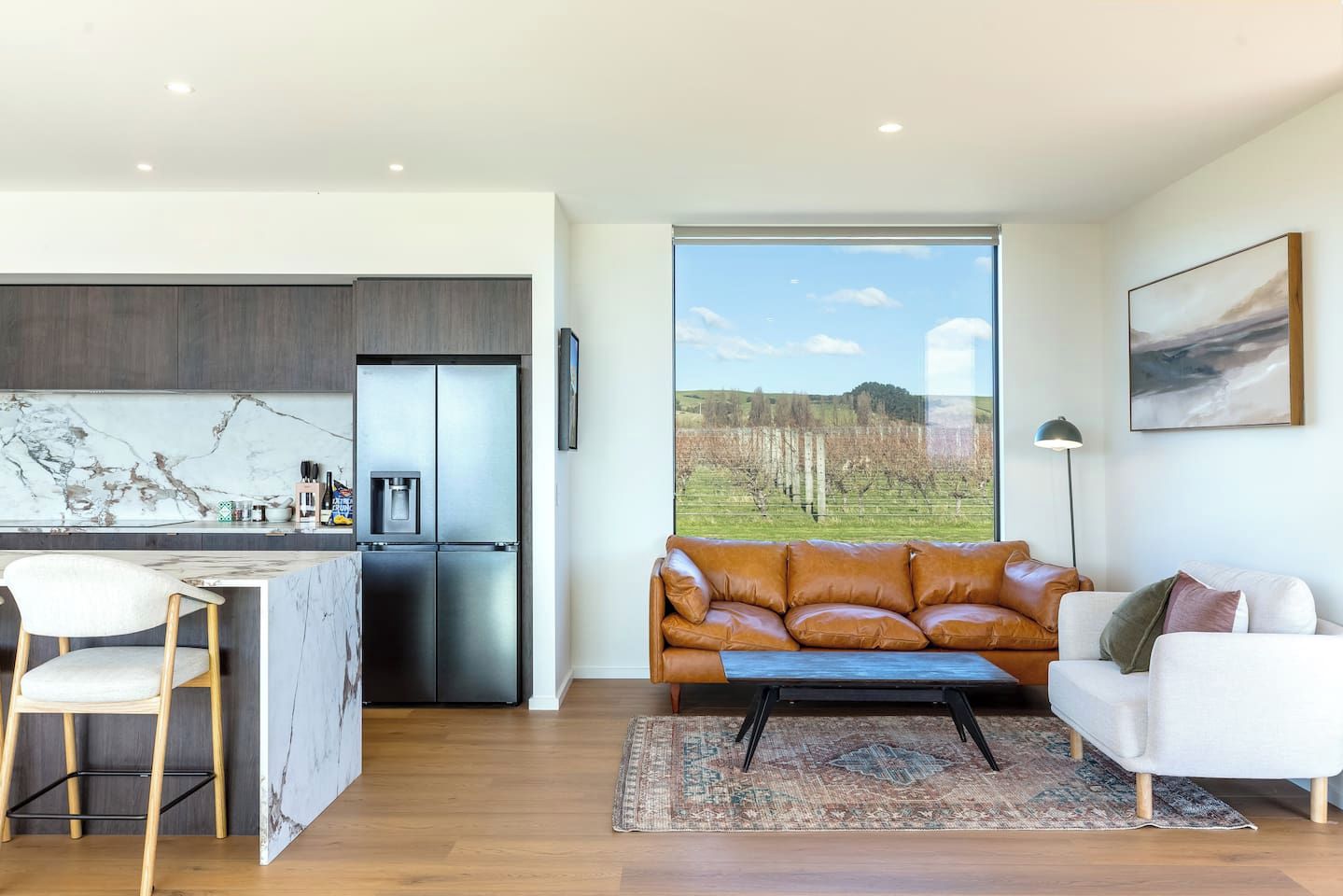 A modern kitchen with a marble backsplash, a stainless steel refrigerator, and a dining area with a white chair.