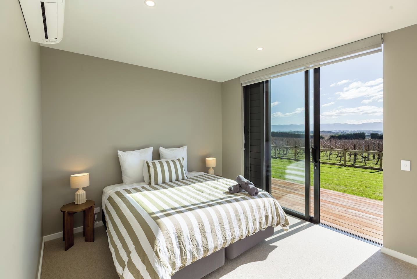 Een slaapkamer met een groot bed, twee nachtkastjes en uitzicht op een wijngaard door een glazen schuifdeur.