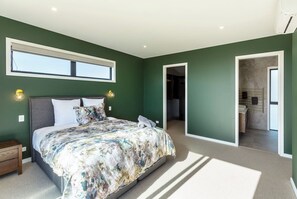 A bedroom with a large bed, a nightstand, a wall-mounted light, and a window.