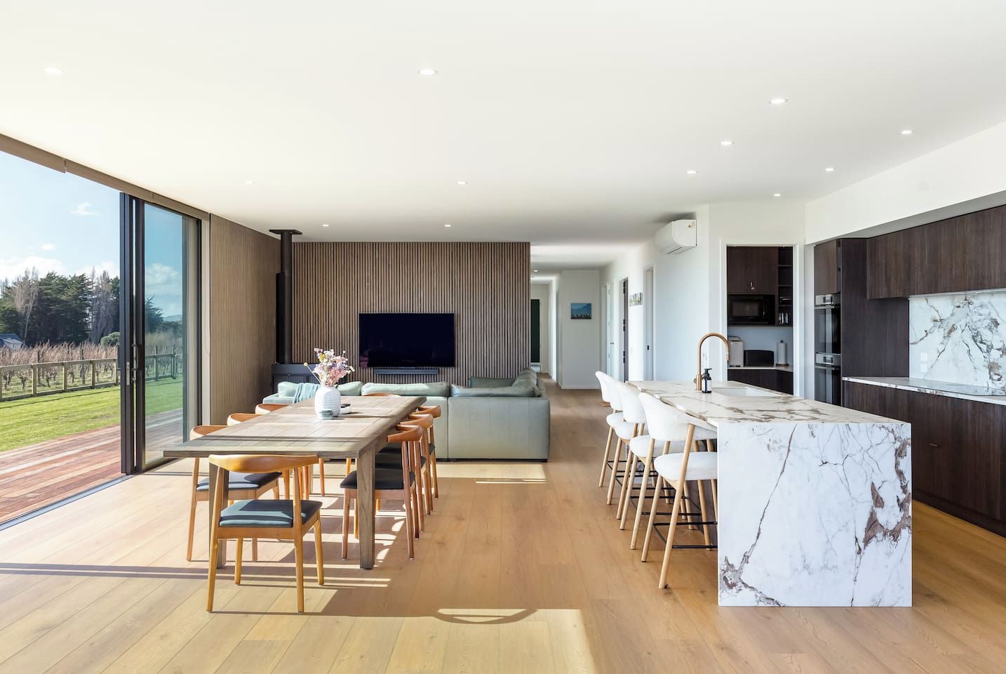 A modern kitchen with a marble countertop, a dining area with wooden chairs, and a large TV screen.
