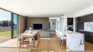 A modern kitchen with a marble countertop, a dining area with wooden chairs, and a large TV screen.