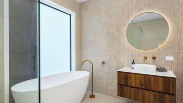 A modern bathroom with a freestanding bathtub, a wooden vanity, and a large mirror with a circular frame.