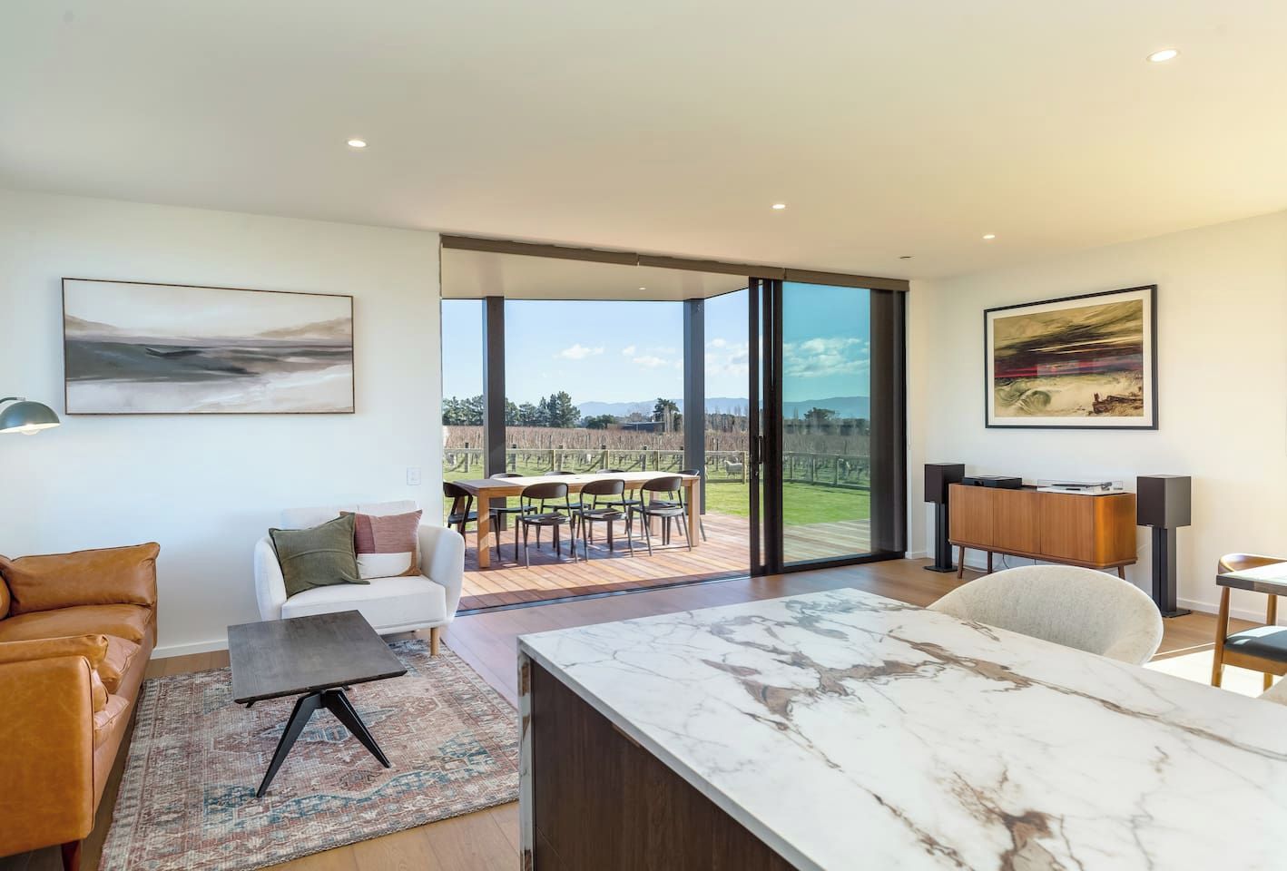 A modern living room with a marble coffee table, a sofa, and a dining area with a view of the outdoors.