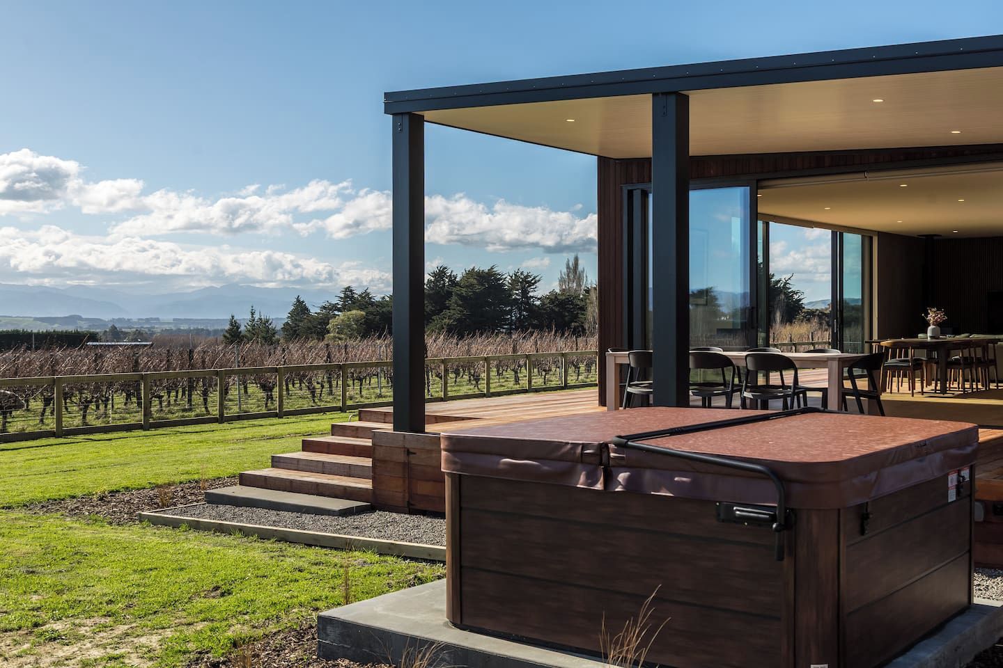 Een modern terras buiten met een jacuzzi, een eethoek en uitzicht op een wijngaard.
