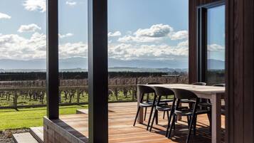 Een terras met een tafel en stoelen, met uitzicht op een wijngaard en verre bergen.