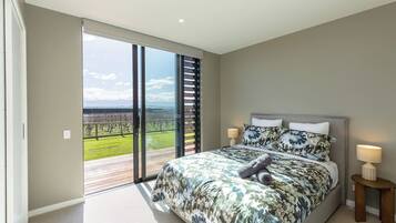 A bedroom with a large bed, a nightstand, a lamp, and a view of a vineyard through a sliding glass door.