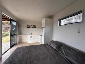 Ein Schlafzimmer mit einem großen Bett, einer kleinen Küchenzeile und einer Schiebetür zu einem Außenbereich.