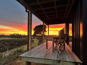 Eine Holzterrasse mit Tisch und Stühlen, mit Blick auf eine Landschaft mit Bäumen und einem Sonnenuntergang.